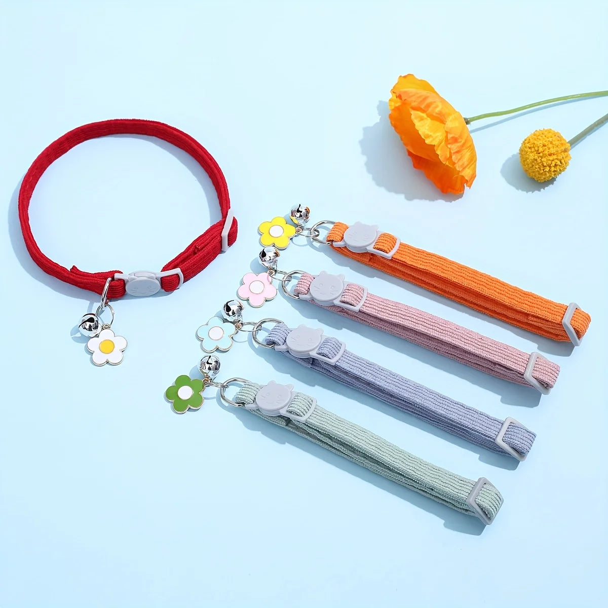 Ensemble de colliers colorés avec des pompons et des breloques florales sur fond bleu clair.

