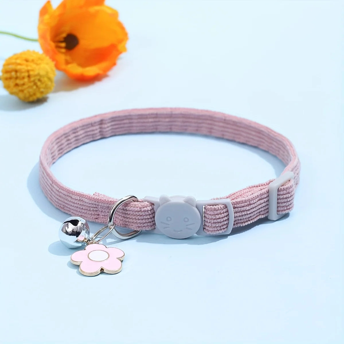 Collier rose avec breloque fleurie et clochette sur fond bleu clair

