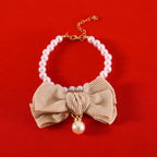 Collier de perles avec un nœud beige et un pendentif en perles sur fond rouge

