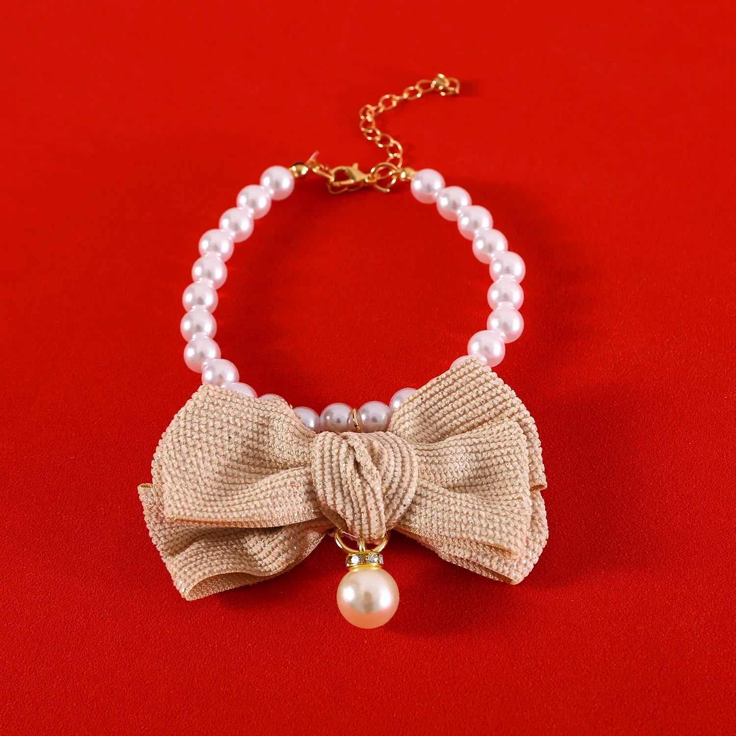 Collier de perles avec un nœud beige et un pendentif en perles sur fond rouge

