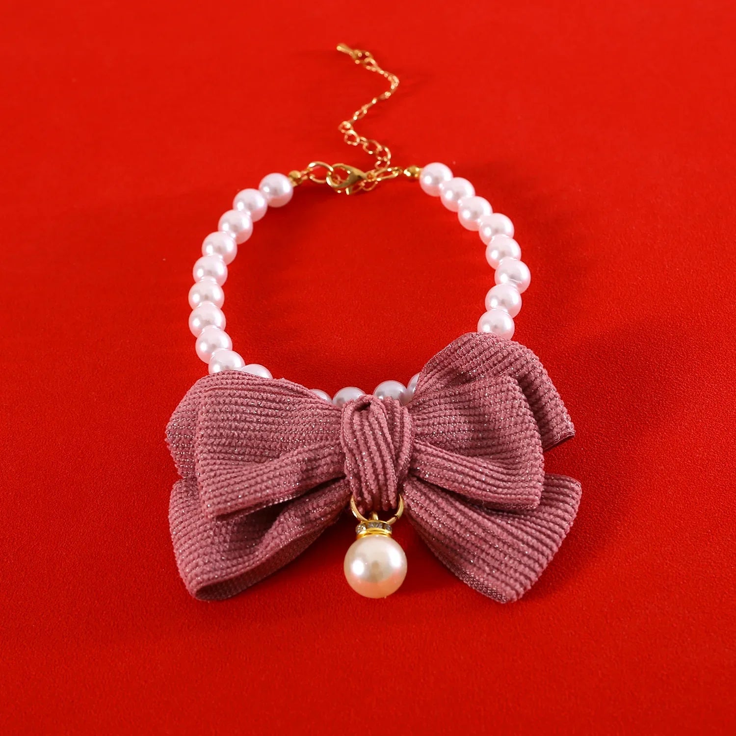 Bracelet avec nœud rose et détails de perles sur fond rouge

