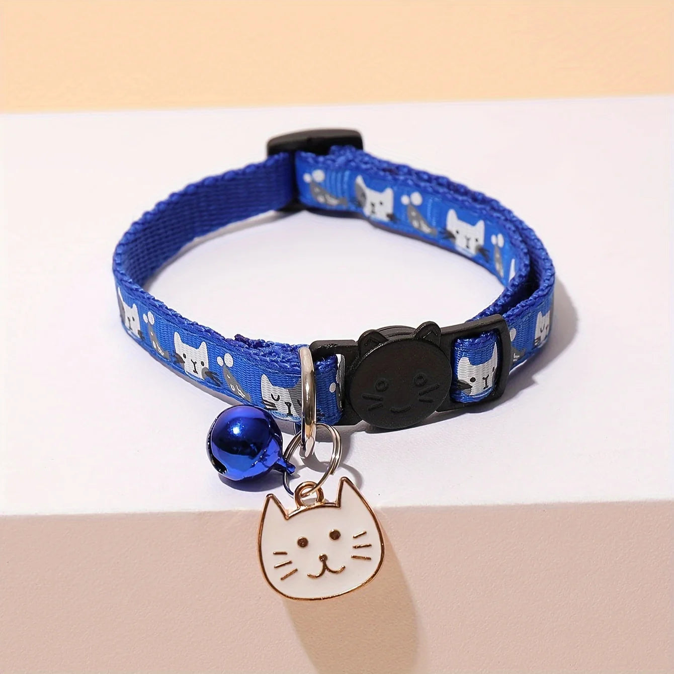 Collier bleu pour chat avec une porte de clochette et une plaque d’empreintes de patte sur fond beige

