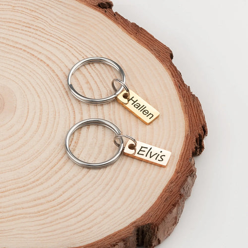 Deux porte-clés avec des noms gravés sur une surface en bois
