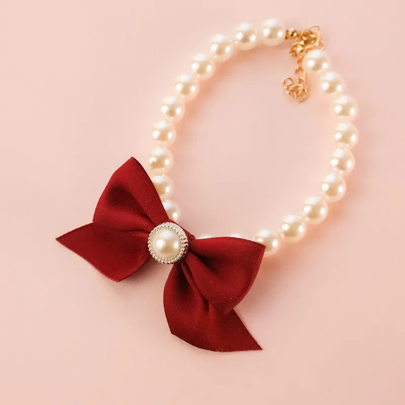 Collier de perles avec un nœud rouge et une perle au centre sur un fond rose

