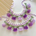 Collier au crochet avec des pompons violets et verts sur fond blanc

