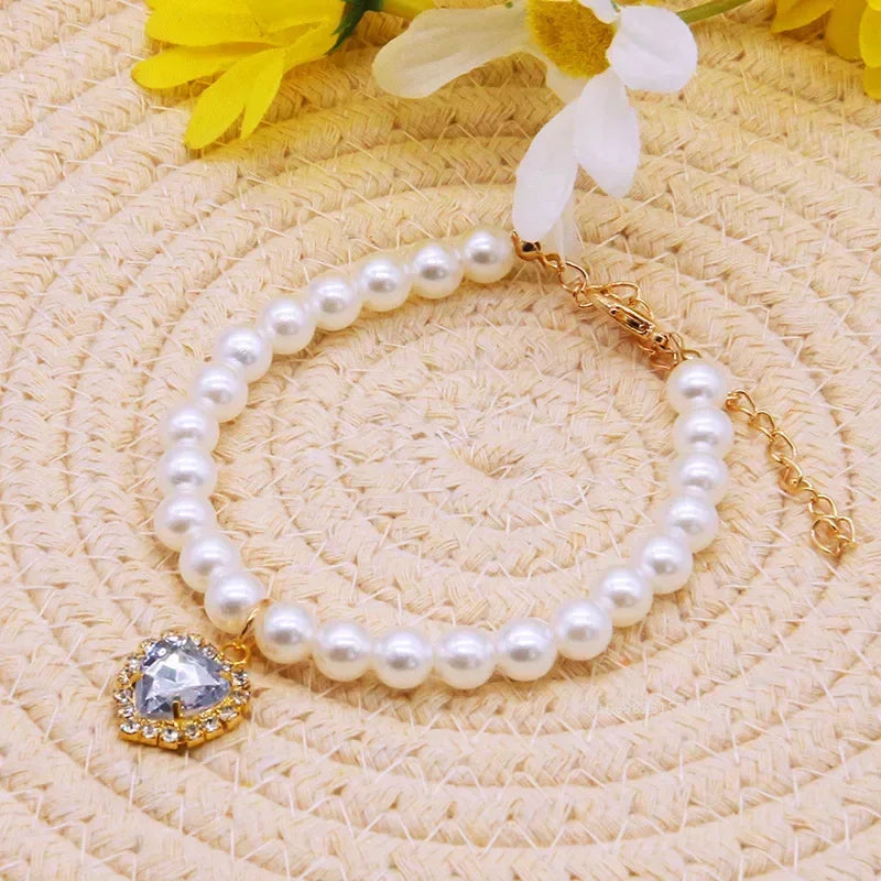 Bracelet en perles avec un pendentif en cristal en forme de cœur sur une surface tissée avec des fleurs.

