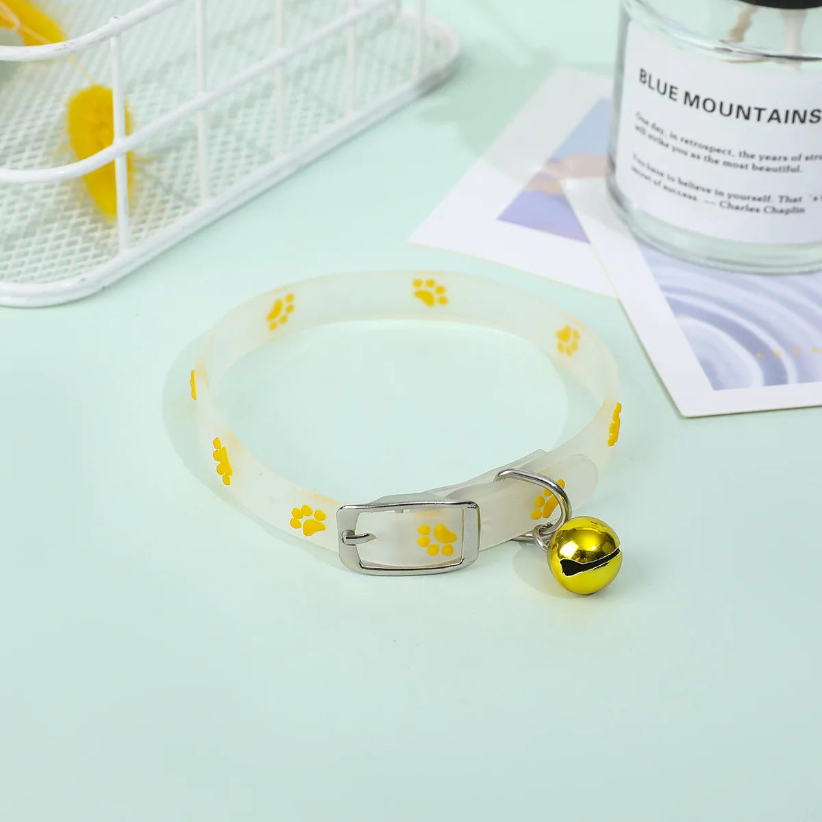 Collier pour chien avec des empreintes de pattes jaunes et une clochette sur une surface vert clair.

