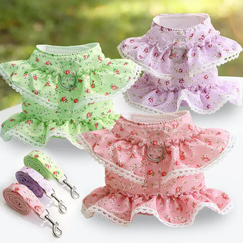 Trois robes florales pour animaux vertes, roses et violettes avec des laisses assorties sur une surface blanche.

