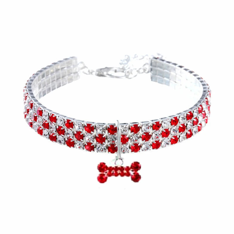 Collier pour chien avec des pierres précieuses rouges et transparentes et un breloque en forme d’os sur fond blanc

