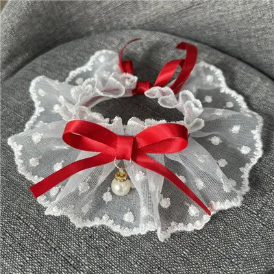 Jarretière en dentelle blanche avec rubans rouges et un pendentif en perle sur une surface grise


