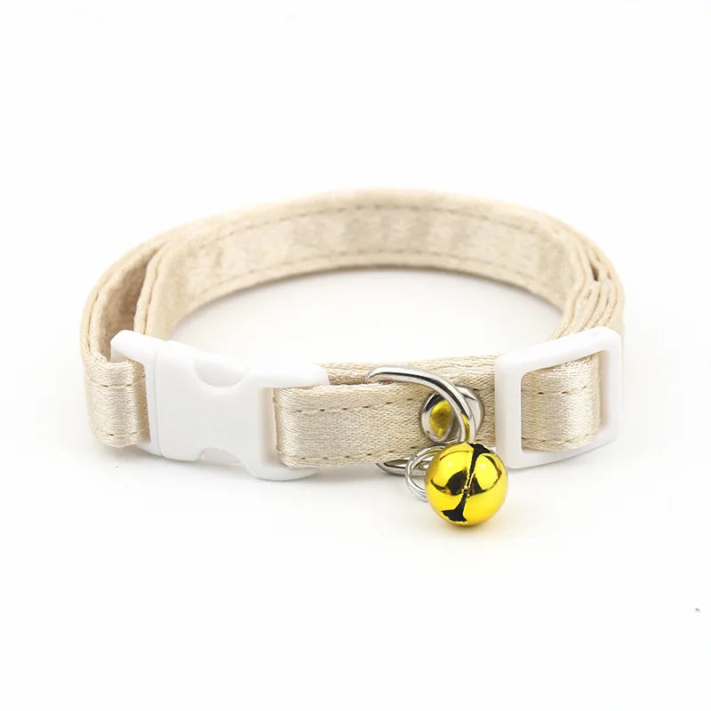 Collier beige avec boucle blanche et clochette jaune sur fond blanc

