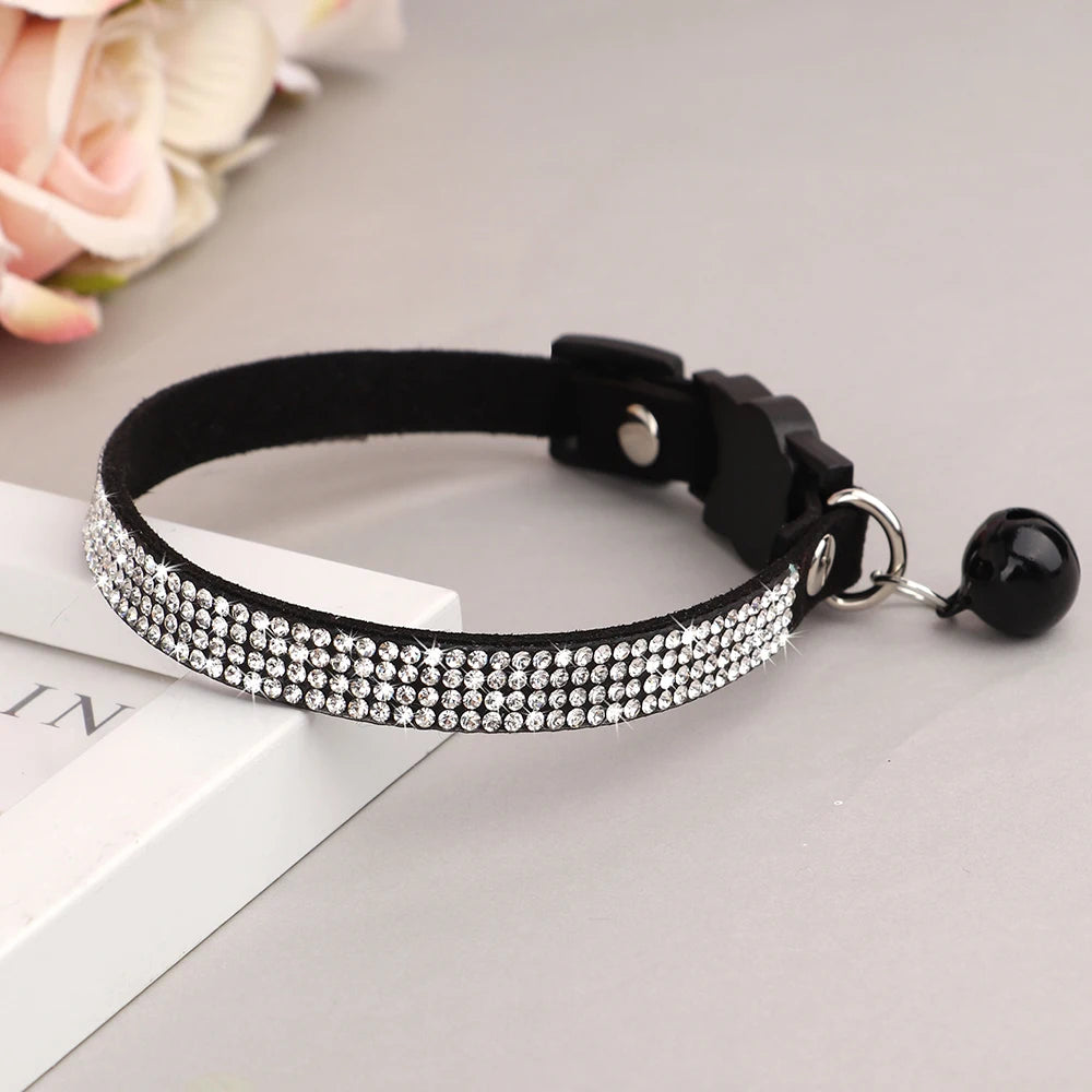 Collier noir pour chat avec des strass sur une surface grise et des fleurs en arrière-plan

