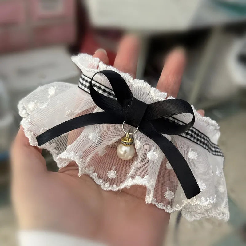 Jarretière en dentelle blanche avec un ruban noir et un charme en perle tenu dans une main.

