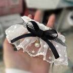 Jarretière en dentelle blanche avec un ruban noir et un charme en perle tenu dans une main.

