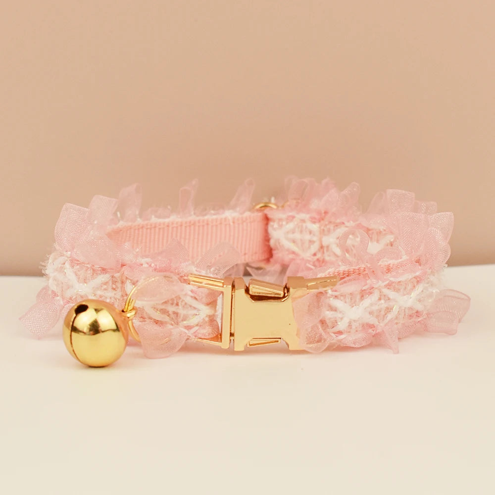 Collier ras-du-cou en dentelle rose avec fermoir et clochette dorés sur fond beige

