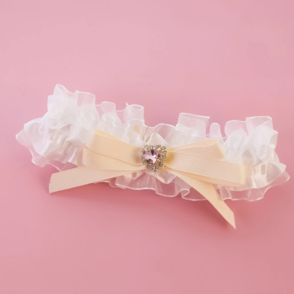 Jarretière en dentelle blanche avec un ruban beige et un cœur décoratif sur fond rose

