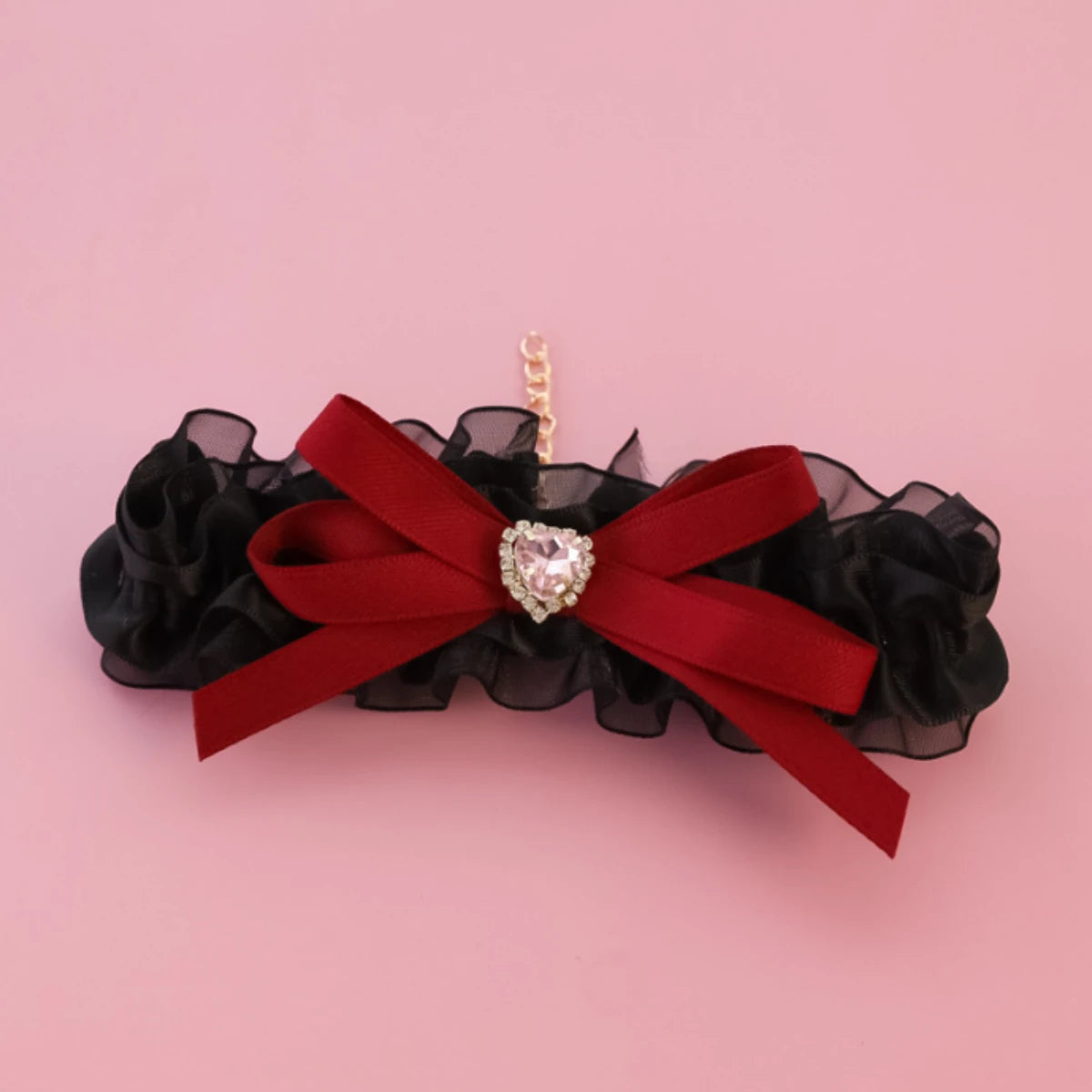Accessoire floral noir avec un ruban rouge et une broche en forme de cœur sur fond rose

