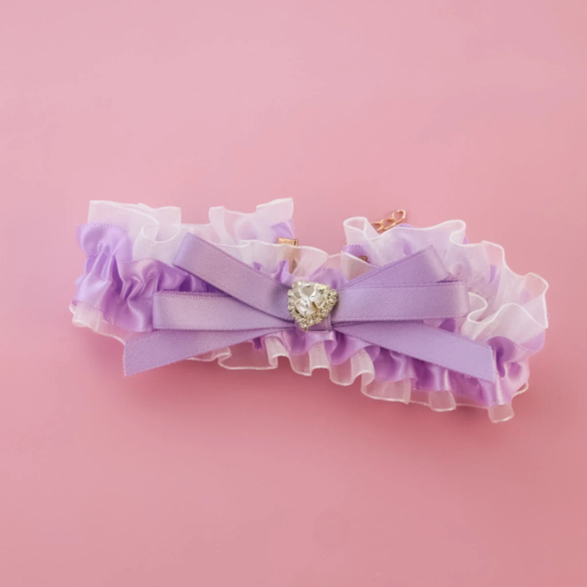 Jarretière violette et blanche à volants avec un nœud décoratif sur fond rose

