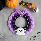 Couronne au crochet sur le thème d’Halloween avec une décoration fantôme sur une surface grise, entourée de citrouilles et de toiles d’araignée.

