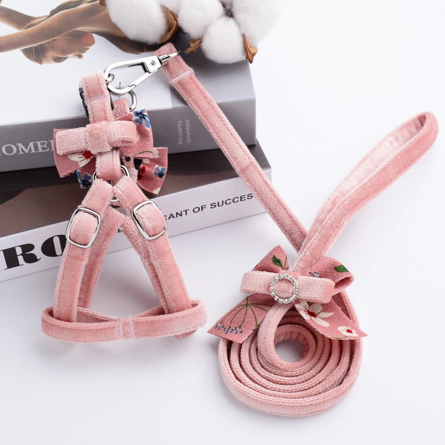Harnais et laisse en velours rose avec des éléments décoratifs sur une surface blanche.

