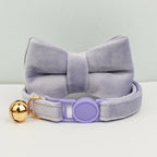 Nœud papillon en velours gris avec une clochette dorée et une boucle violette sur fond gris clair

