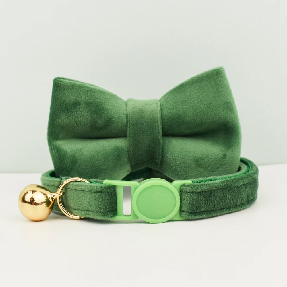 Nœud papillon en velours vert avec une clochette dorée et une pince verte sur fond blanc
