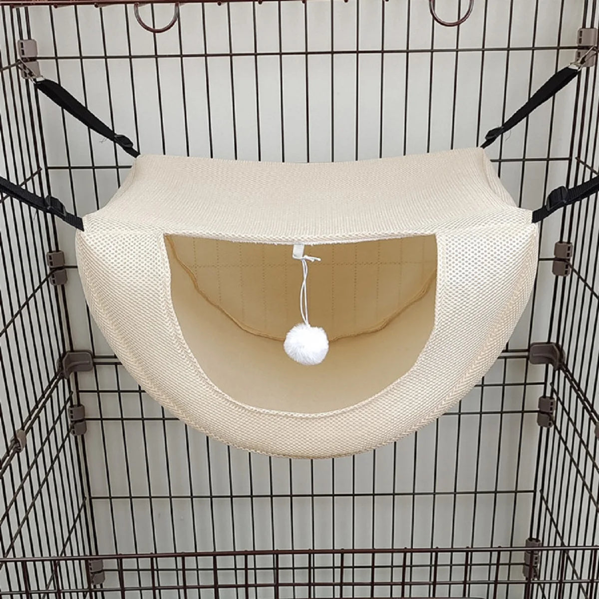 Hamac beige pour animaux avec une boule blanche suspendue à l’intérieur d’une cage en fil métallique
