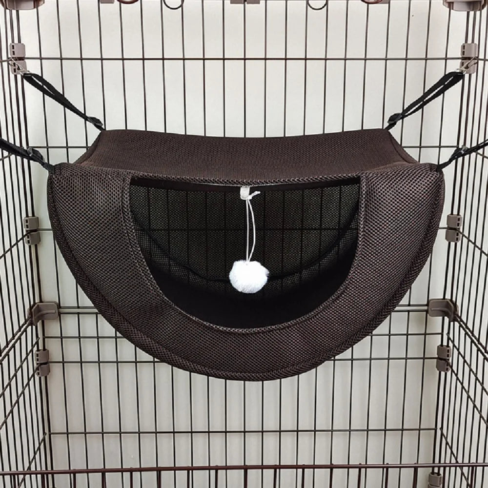 Hamac marron pour animaux avec un pompon blanc suspendu à l’intérieur d’une cage en fil de fer.

