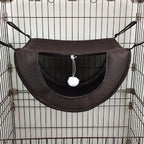 Hamac marron pour animaux avec un pompon blanc suspendu à l’intérieur d’une cage en fil de fer.
