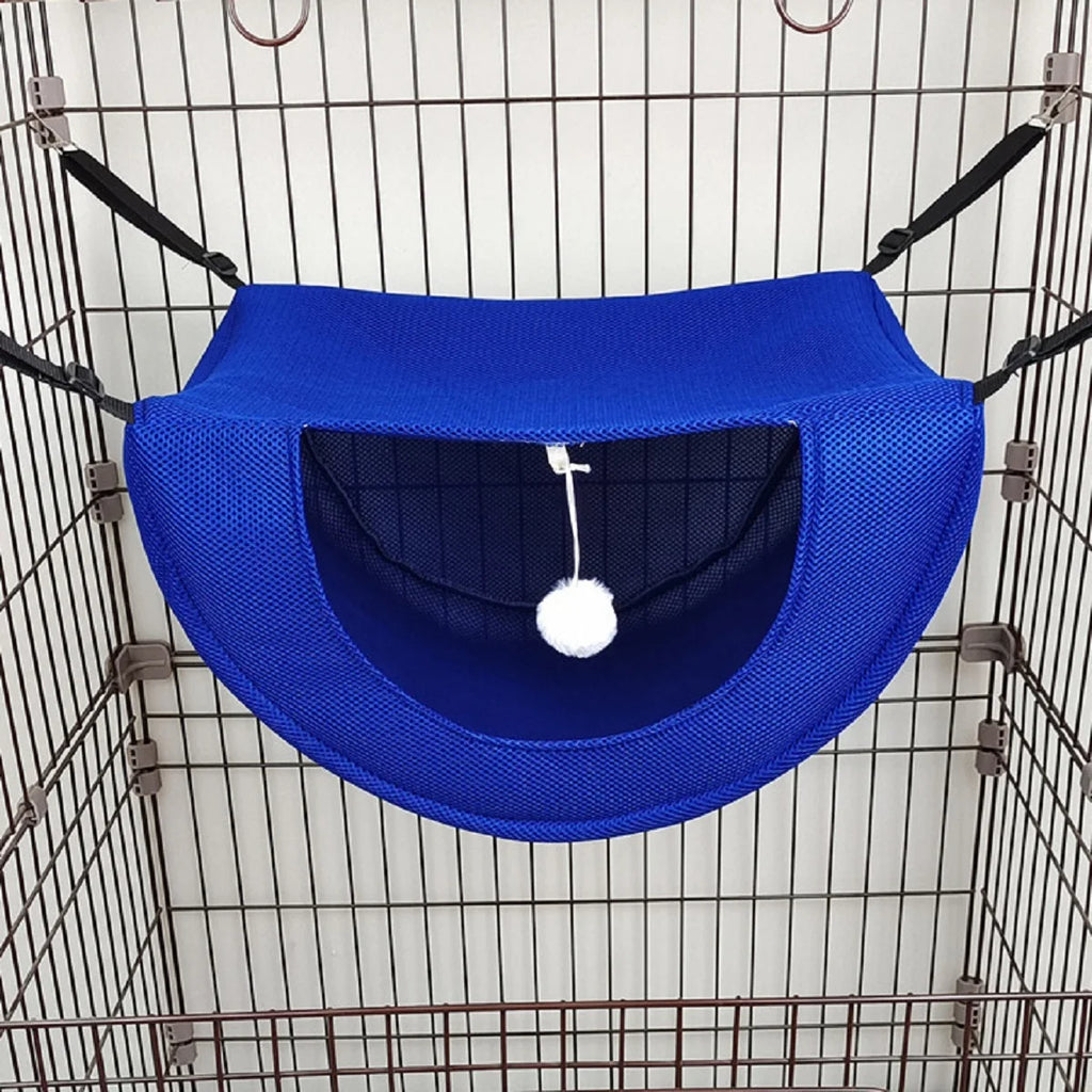 Hamac bleu pour animaux avec un pompon blanc suspendu à l’intérieur d’une cage en fil de fer.
