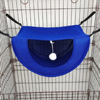 Hamac bleu pour animaux avec un pompon blanc suspendu à l’intérieur d’une cage en fil de fer.
