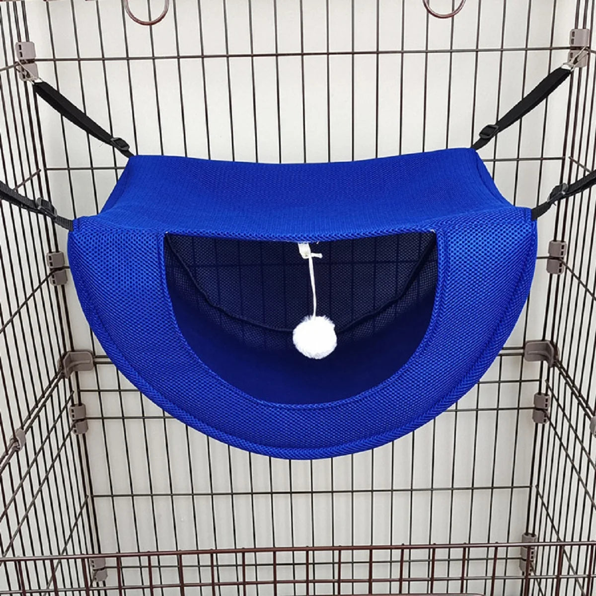 Hamac bleu pour animaux avec un pompon blanc suspendu à l’intérieur d’une cage en fil de fer.
