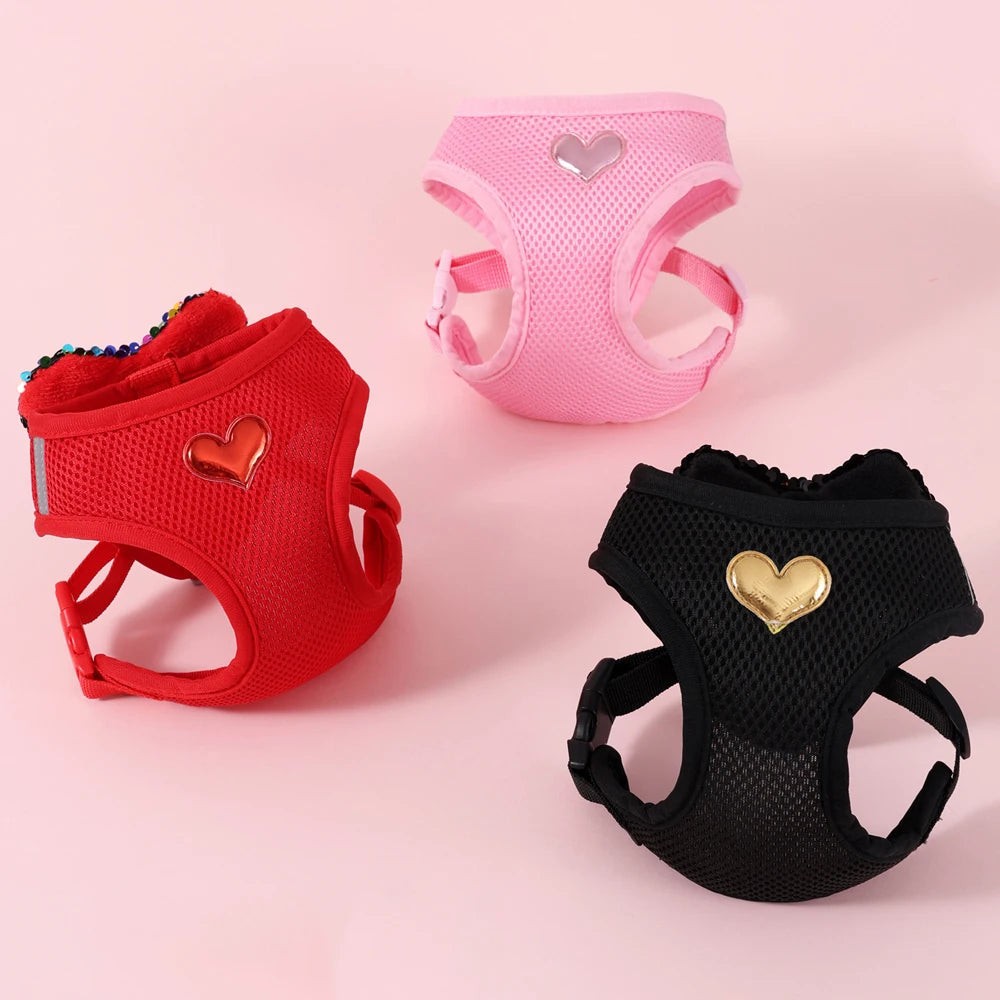 Trois harnais pour animaux en rouge, rose et noir avec des motifs en forme de cœur sur fond rose

