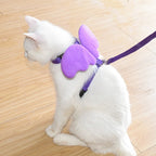 Chat blanc portant un harnais violet et des ailes de papillon sur un sol en bois

