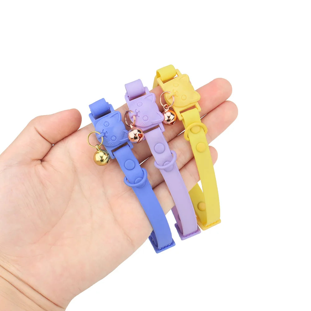 Trois colliers colorés avec des cloches tenus dans une main sur un fond blanc.

