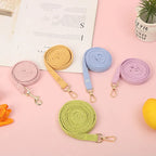 Un ensemble de laisses colorées sur une surface rose avec un livre et une plante en arrière-plan.


